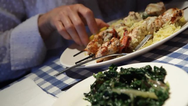 A woman dining at a Greek restaurant garnishes her horta and shish kabob with lemon.