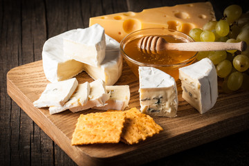 Slate board with various cheese and a glass of red rose wine. Brie. Camembert. Gouda, Masdaam, Roquefort, Cheddar and grapes on a wood with nuts, honey, crackers, blue cheese. Italian, French cheese.