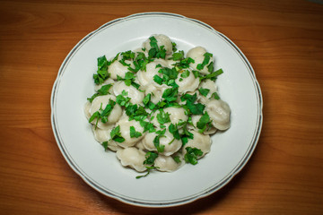 Boiled prepared homemade russian dumplings or pelmeni with beef meat on the white plate with fresh parsley