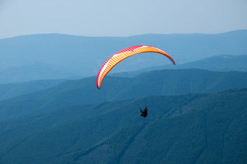 Paragliding in the sky. One paraglider fly over a mountain valley in summer sunny day. Carpathians, Ukraine.