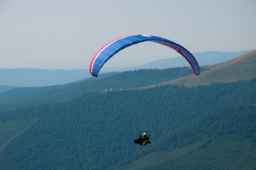 Paragliding in the sky. One paraglider fly over a mountain valley in summer sunny day. Carpathians,...