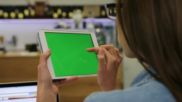 Young beautiful woman using tablet with green screen sitting in the cafe, swipe pictures. Close-up. Chroma key