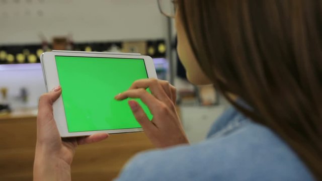 Young attractive woman using tablet with green screen sitting in the cafe, swipe pictures, news. Close-up. Chroma key
