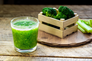 Green vegetable smoothie in glass at wooden background
