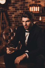 Confident bearded handsome man in black suit with glass of whisk