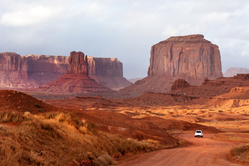Fototapeta na wymiar White car driving through the rocks of Monument Valley park, Arizona 