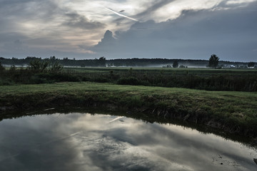Village landscape with a pond and streaks of mist in Poland.