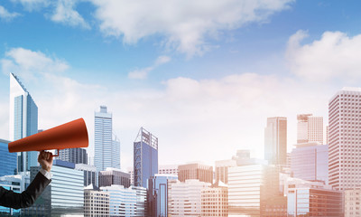 Naklejka premium Hand of businesswoman holding red paper trumpet against cityscape background