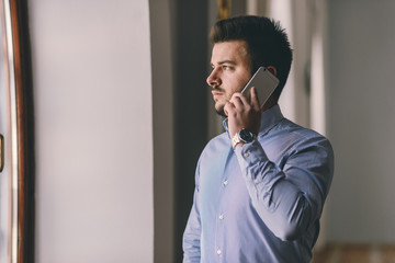 Young businessman talking on phone while watching trough window