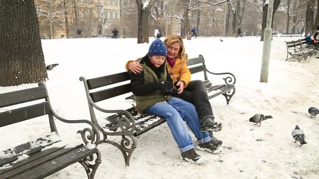 Mother with son sitting on a park bench, a snowy winter day
