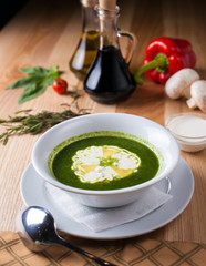 white plate with soup green, poured sour cream on wooden table surrounded by decor