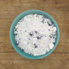 Top view of a bowl of blueberry muffin mix on an old wood cutting board.