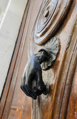 A solid metal iron door knocker sculpted into a hand, on an old wooden ornate door.