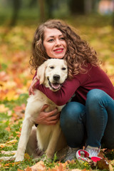 Close-up of curly woman sitting with her dog in autumn leaves outdoors