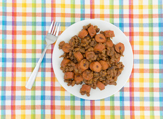 Top view of beans and hot dogs on a plate with a fork to the side atop a colorful place mat.