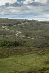 Assynt Peninsula, Scotland - June 7, 2012: Under blue-gray-white sky over a green bare landscape, the B869 road meanders over rocky hills and past pastures.