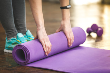 Close-up of attractive young woman folding yoga or fitness mat a - obrazy, fototapety, plakaty