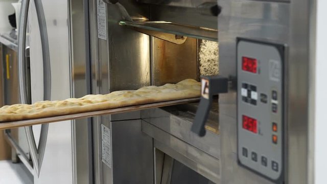 Baker pulling out of the electric oven a focaccia and then put it back in