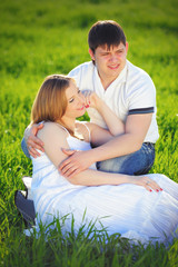 young pregnant couple sitting on green grass in spring