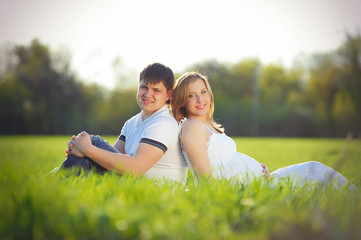 young pregnant couple sitting on green grass in spring