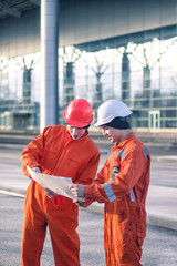team of  young engineers discussing a construction project. The wear overalls and safety helmets. Business modern background
