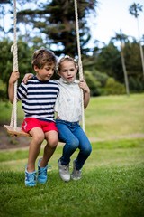 Boy and girl sitting on a swing in park