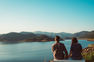 a couple stand hugging, embracing, overlooking a lake with mountains in the background. Traveling together, adventure