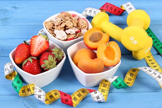 Fresh fruits, wheat and rye flakes, dumbbells and centimeter, healthy and sporty lifestyle