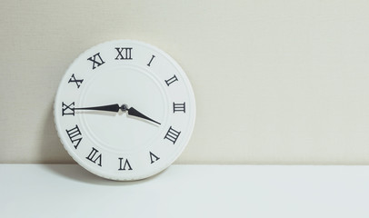 Closeup white clock for decorate show a quarter to four p.m. or 3:45 p.m. on white wood desk and cream wallpaper textured background with copy space