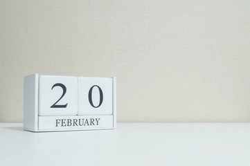 Closeup white wooden calendar with black 20 february word on blurred white wood desk and cream color wallpaper in room textured background with copy space in selective focus at the calendar