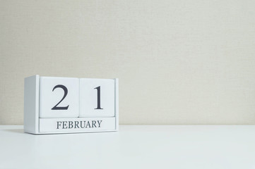 Closeup white wooden calendar with black 21 february word on blurred white wood desk and cream color wallpaper in room textured background with copy space in selective focus at the calendar