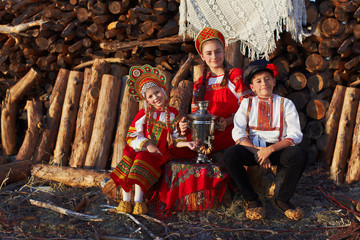 Three adorable kids in folk Russian costume and headdresses with samovar and in ancient shoes