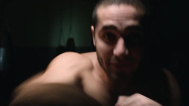 Strong mixed martial arts fighter throwing punches at camera in darkness in slow motion