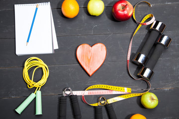 Heart, fruit and dumbbells. Fitness, healthy lifestyle on a black wooden background