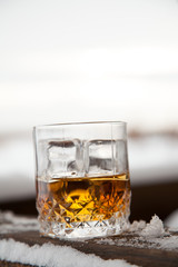 glass of whiskey with ice in snow on winter background.