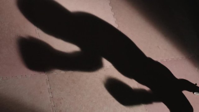Slow motion shot of moving shadow on the floor of ring of male boxer throwing punches in boxing gloves