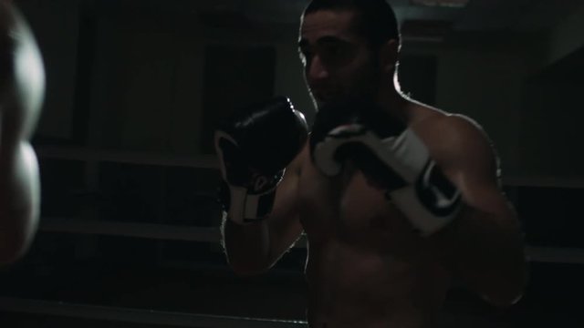 Aggressive MMA athlete in boxing gloves kicking his opponent and throwing punches during fight in slow motion