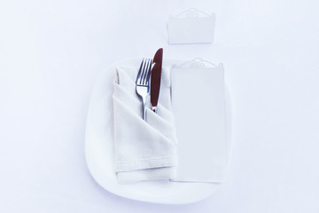 Plate, cutlery in textile napkin and menu plate isolated on white