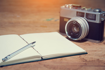 Paper notebook with pen and vintage camera on a wood table