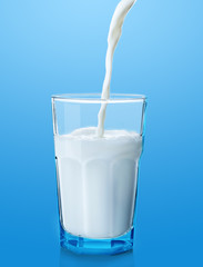 Pouring milk into glass on blue background