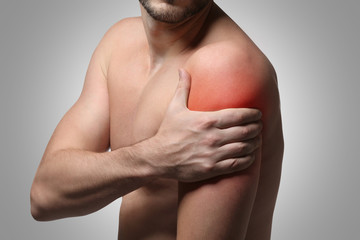 Young man suffering from shoulder pain on gray background. Health care concept