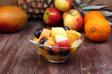 Bowl of healthy fresh fruit salad on wooden background.