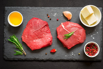 Raw beef steaks and rosemary on a black slate board. Top view