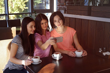 Cheerful young women taking selfie while drinking coffee in cafe