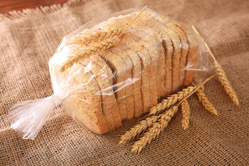 Sliced bread in plastic bag on sackcloth with wheat spikes closeup