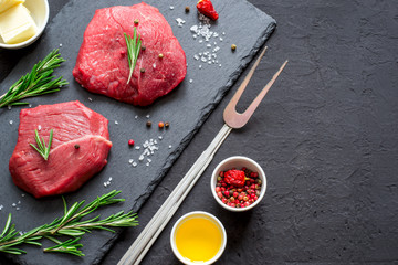 Raw meat beef steaks on black slate board, spices and ingredient