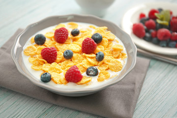 Tasty cornflakes with raspberries and blueberries on gray wooden background