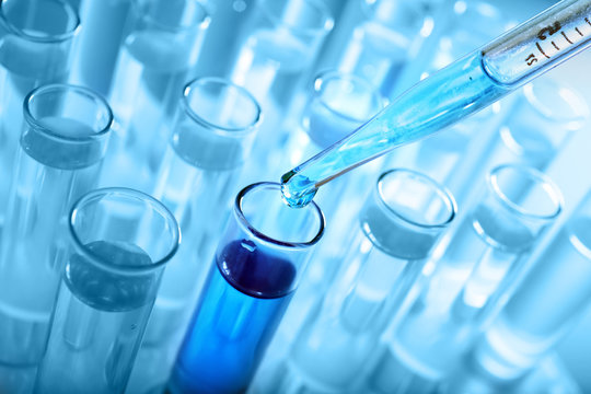 Closeup of a pipette dropping a sample into a test tube on blue background