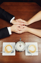 Hands of the newlyweds and two cups of cappuccino