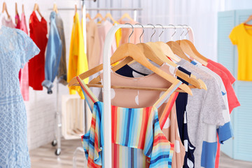 Fashionable clothes hanging on rack at room